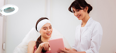 a woman pointing at a pink tablet in a consultation with a beautician