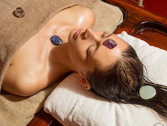 woman receiving a relaxing stone therapy treatment with various gemstones placed on her forehead and chest on a spa table