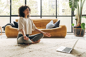 woman meditating in cozy living room with laptop on floor and yellow sofa surrounded by plants serene atmosphere for healthy lifestyle and self improvement journey 17 techniques for mindfulness